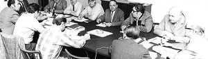 Old black and white photo of 12 men in suits seated around a conference table